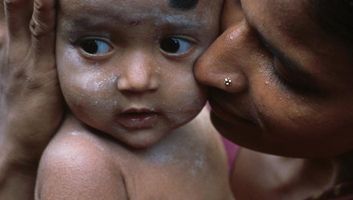 a mother holds and kisses the cheek of her infant