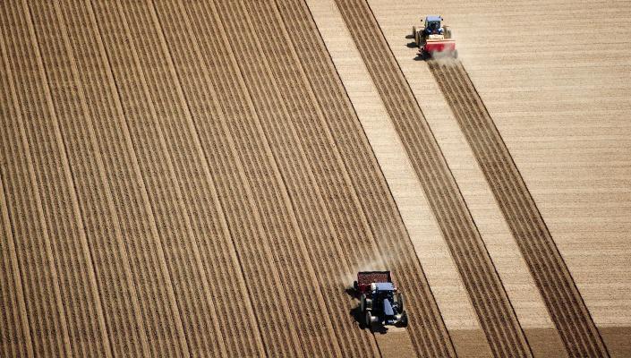 Aerial view of 2 tractors planting potatoes in the fertile farm fields of Idaho, during the spring.