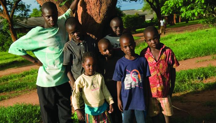 a man and 6 children stand in the shade of a tree in Macha, Zambia