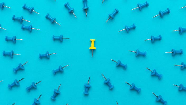 A yellow pushpin surrounded by blue pushpins, which all point toward the yellow pin