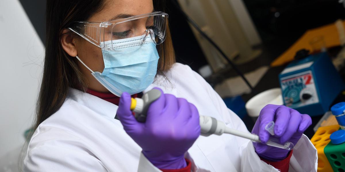 Woman wearing goggles, mask, and gloves, working with laboratory equipment