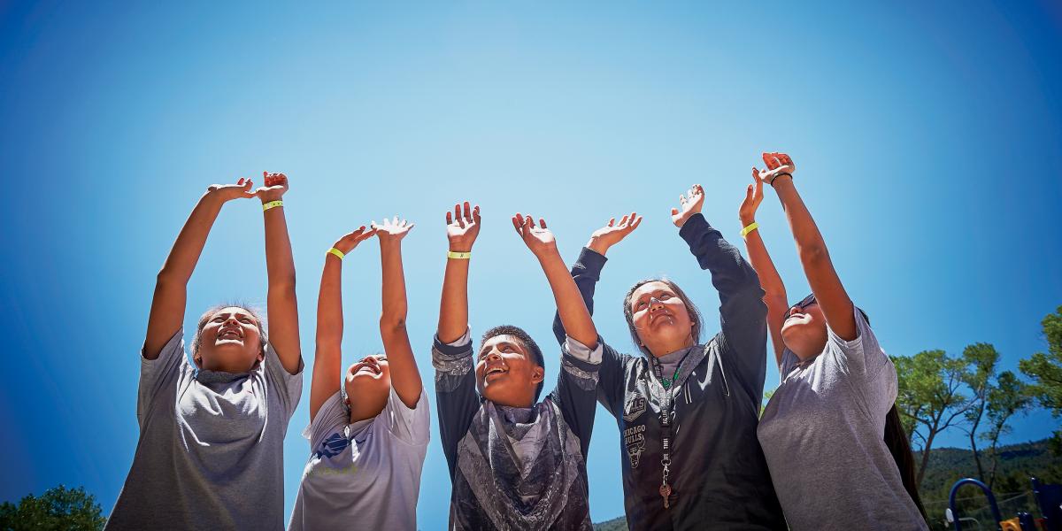 A group of teens raise their hands to the sky in celebration.