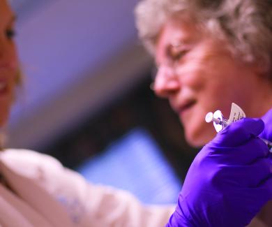 a nurse wearing purple gloves prepares to vaccinate an older adult woman