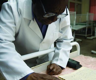 Clinician Redson Makasa, wearing a lab coat, reviews a paper ledger of measles cases