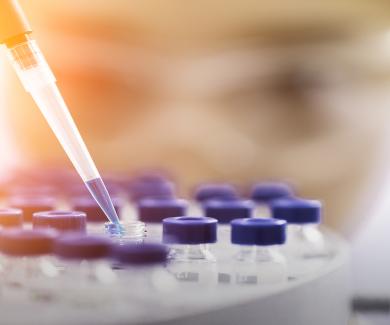 photograph of scientist wearing goggles pipetting liquid into vials