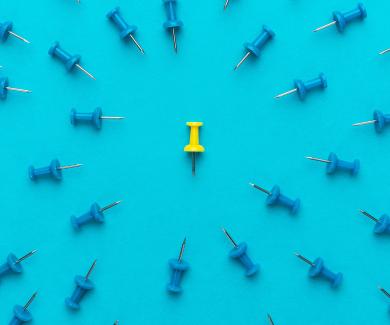 A yellow pushpin surrounded by blue pushpins, which all point toward the yellow pin